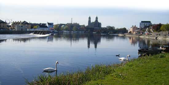 the river shannon in athlone with swans in the foreground - town bridge, athlone castle and saint peter and paul's church in the background