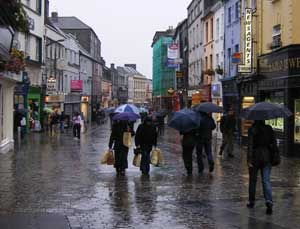 Shoppers with umbrellas on a wet Irish street in June